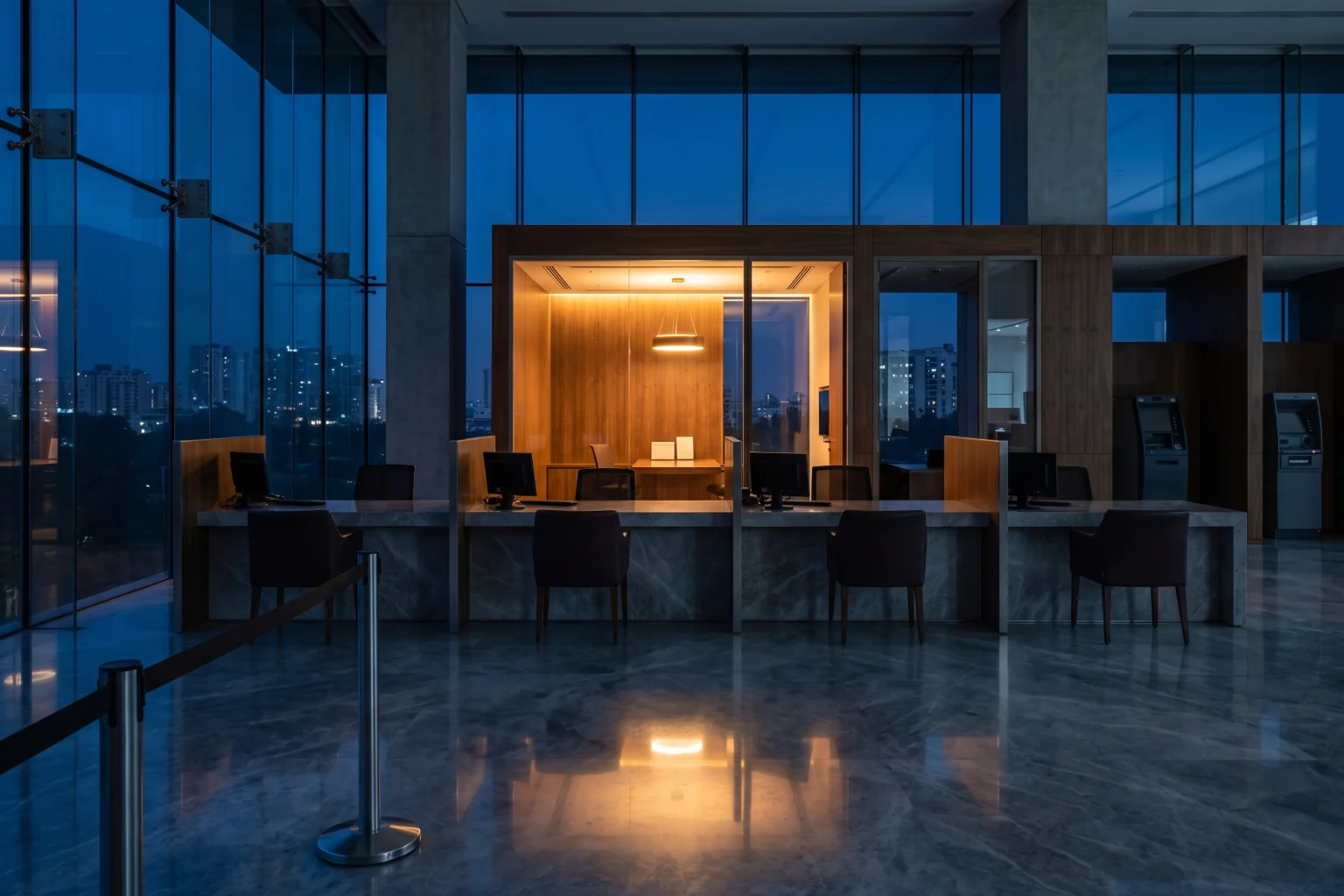 A bank service floor at blue hour, the counter closed and one consultation room lit behind it.