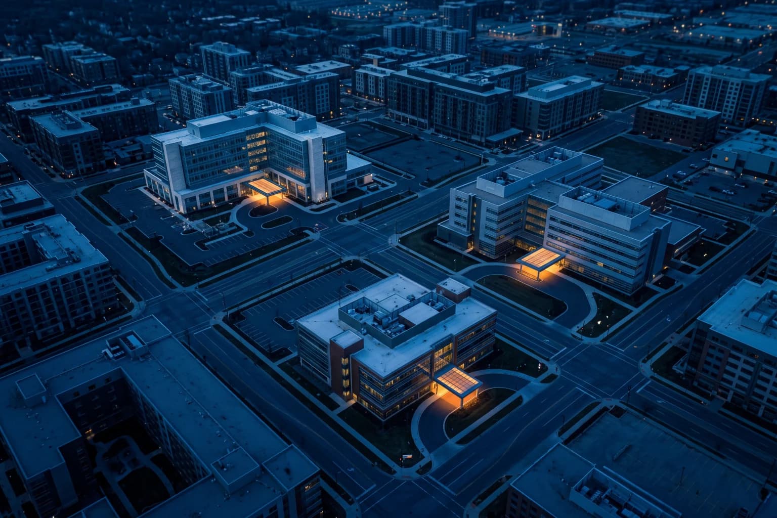 An aerial view at blue hour of three separate hospital buildings, each with a lit entrance.