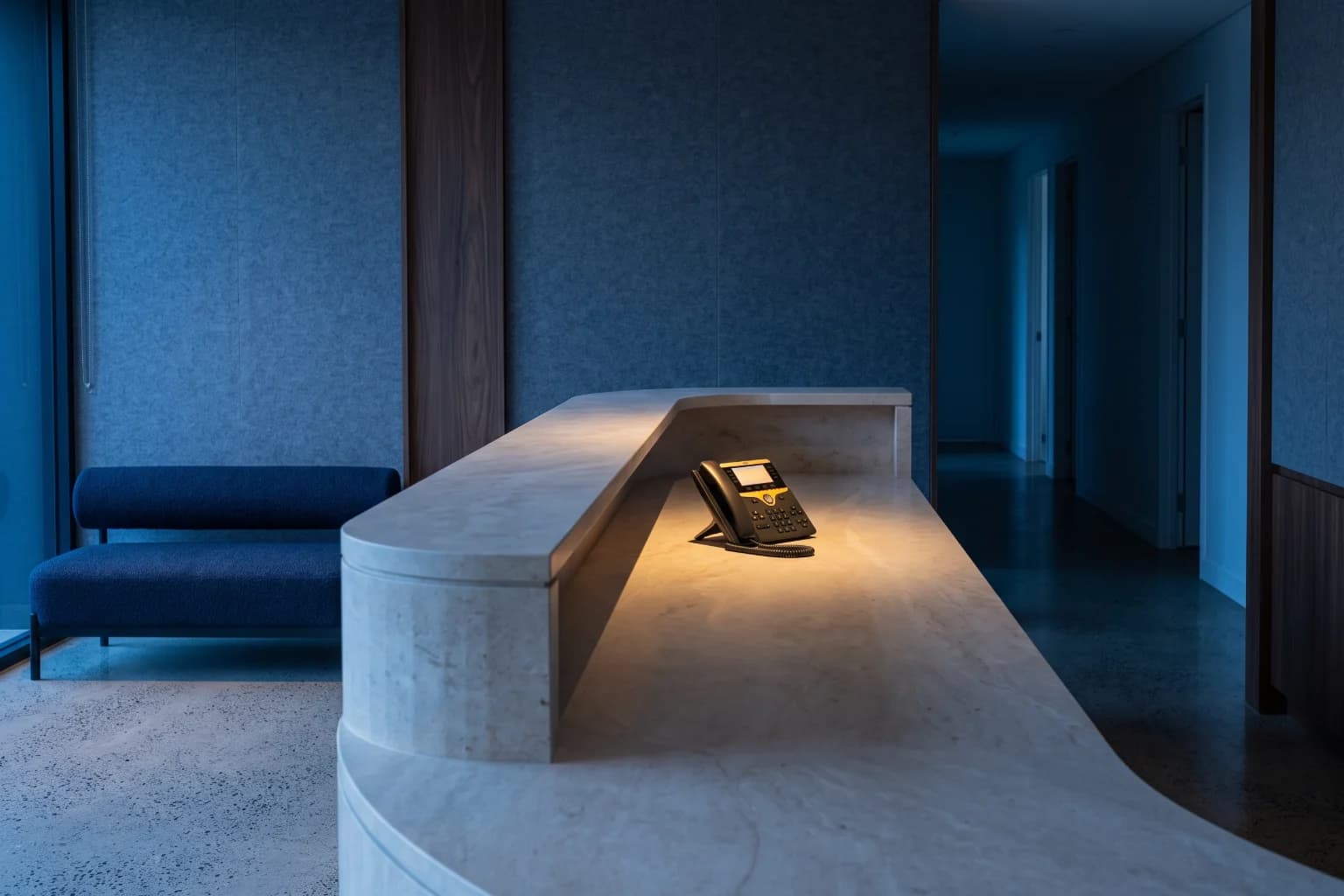 A clinic reception at dusk, the desk empty and a single telephone lit on the counter.