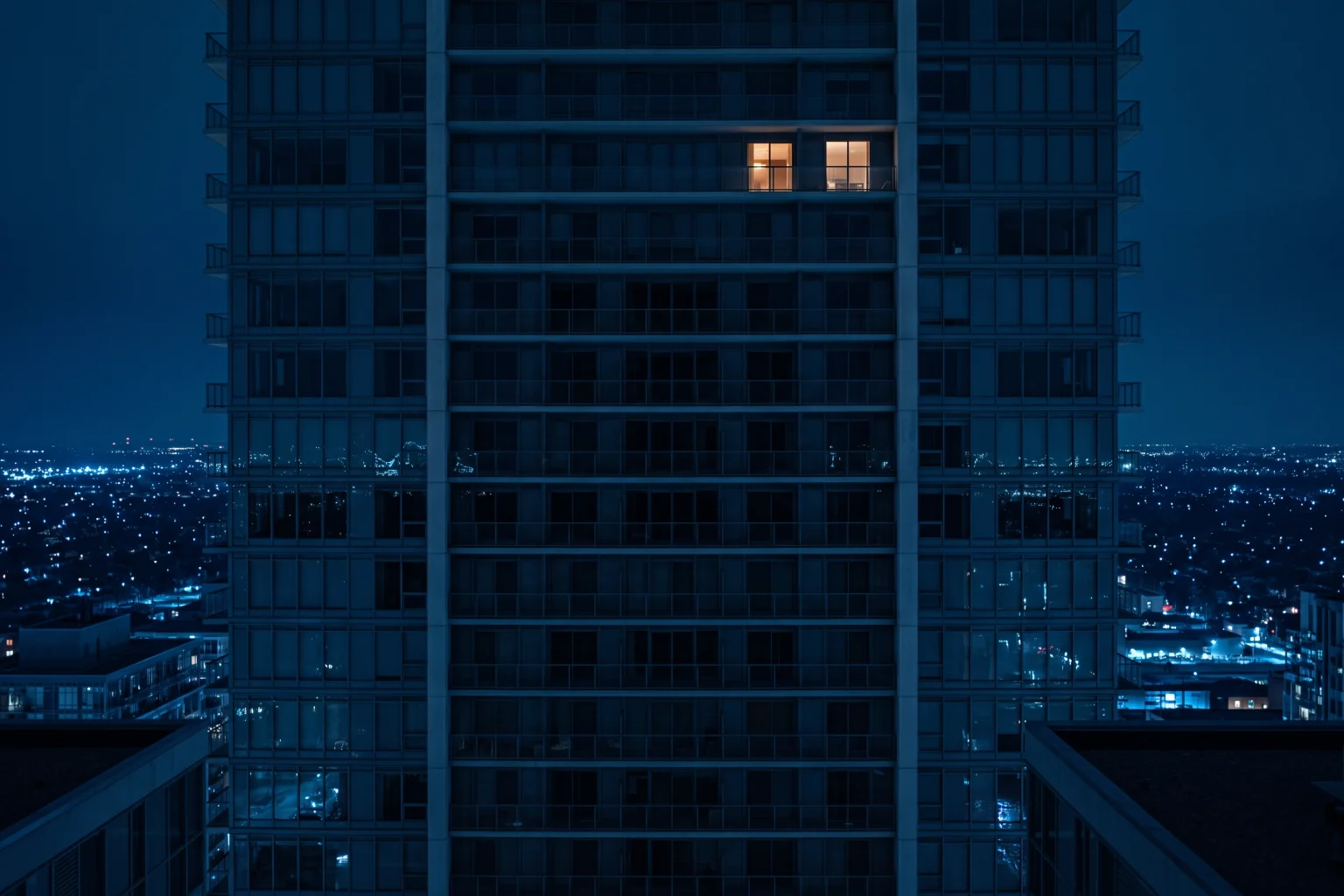 A residential tower at night with a single window lit high on the facade.